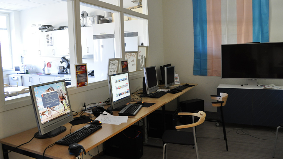 Långt
skrivbord med fyra datorer, en tv på väggen bredvid.