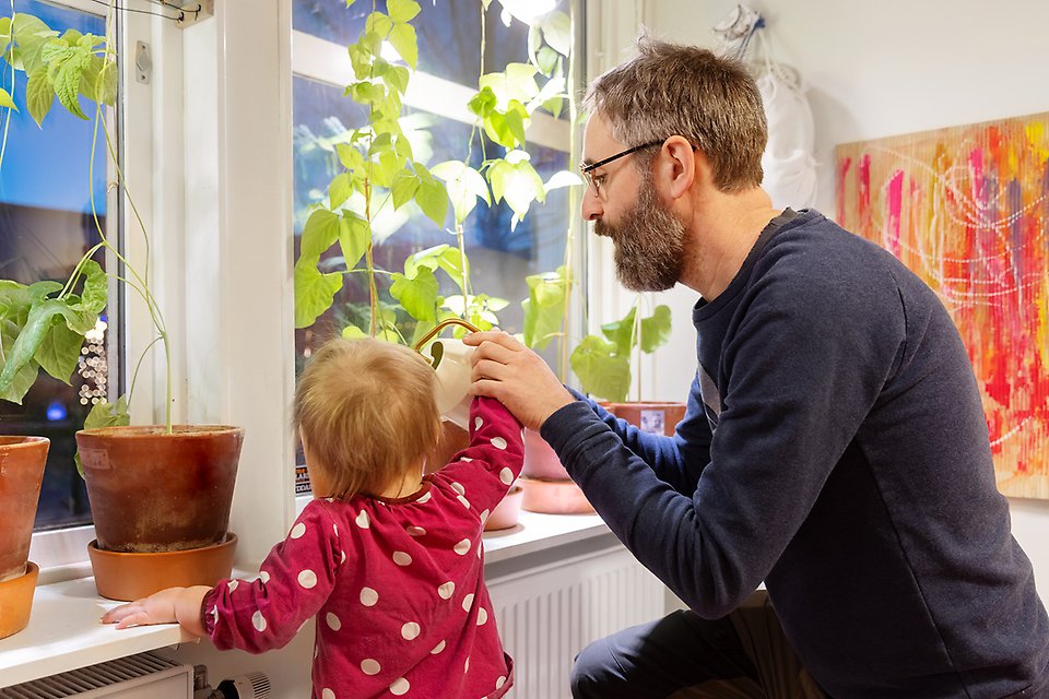 Förskollärare och barn vattnar växter i förskolans fönster.